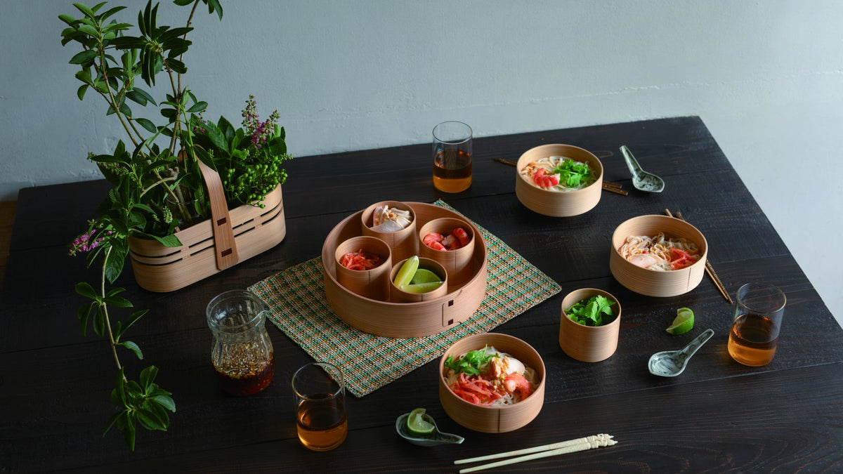 曲げわっぱの器に麺料理やえびなどの具材を盛りつけた食卓